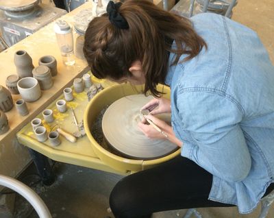 Allison smiling in an art studio, her hands and green sweatshirt smudged with charcoal, beside a large charcoal drawing.